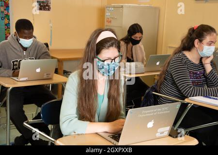 École secondaire, salle de classe, étudiants au travail sur un bureau utilisant un ordinateur portable, tous portant un masque facial pour protéger contre l'infection Covid-19 Banque D'Images