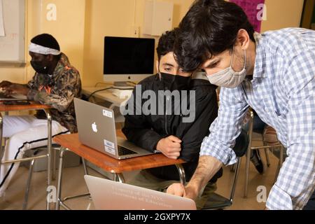 Éducation secondaire enseignant de sexe masculin se penchant pour montrer quelque chose d'étudiant de sexe masculin sur ordinateur portable, tous deux portant un masque facial pour protéger contre Covid-19 Banque D'Images