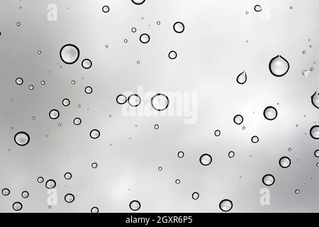 L'eau tombe contre une fenêtre en verre sur un ciel gris Banque D'Images