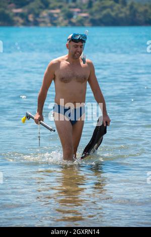 Jeune pêcheur souriant avec de l'équipement dans l'eau peu profonde de la mer tout en se préparant pour la pêche sous-marine vacances actives concept Banque D'Images