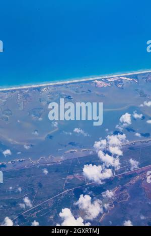 Vue en avion sur la terre à côté de l'océan avec de petits nuages blancs Banque D'Images