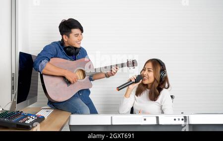 Une jeune femme asiatique chante tout en jouant un clavier électrique devant un mur blanc. Son petit ami joue de la guitare ensemble. Musiciens produisant de la musique en pro Banque D'Images