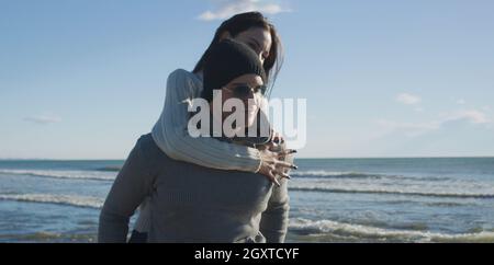 Les hommes Donner Piggy Back Rides au coucher du soleil par la mer, le temps d'automne Banque D'Images