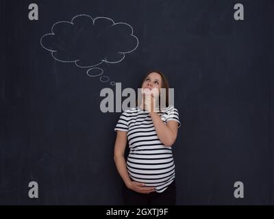 Jeune femme enceinte de penser à des noms pour l'enfant qu'à les écrire sur un tableau noir Banque D'Images