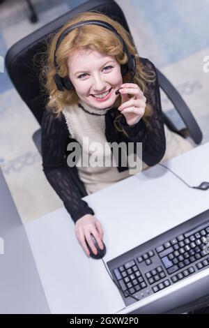 Vue de dessus d'une jeune femme souriante de l'opérateur de centre d'appel fait son travail avec un casque Banque D'Images