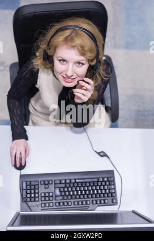 Vue de dessus d'une jeune femme souriante de l'opérateur de centre d'appel fait son travail avec un casque Banque D'Images