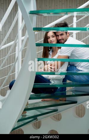 Jeune couple détendue sur verre escaliers en spirale à l'intérieur villa maison moderne Banque D'Images