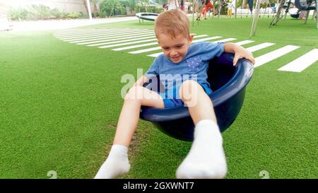 Portrait d'un garçon souriant et gai tournant dans un carrousel sur l'aire de jeux pour enfants au parc. Banque D'Images