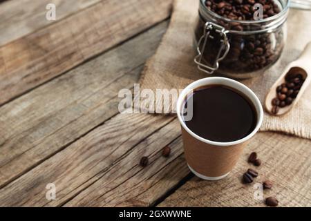Concept de petit déjeuner au café avec une tasse de papier de café noir expresso, café torréfié sec grains dans le pot en verre et cuillère à l'ancienne table en bois Banque D'Images
