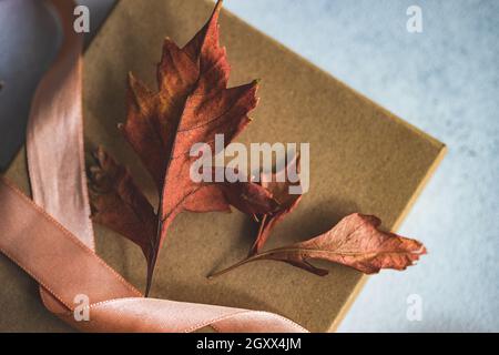 Gros plan d'une boîte cadeau automnale attachée avec un ruban et des décorations de feuilles d'automne séchées sur une table Banque D'Images