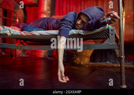 La femme drogué dort sur le lit dans le coin-détente, intérieur de shebang sur fond, coin-détente.Problème de stupéfiants, dépression éternelle des gens grossieux Banque D'Images