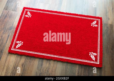 Tapis de bienvenue blanc rouge des fêtes avec coins en Holly sur fond de plancher en bois. Banque D'Images