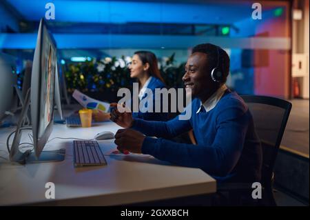 Deux managers souriants travaillent dans le bureau de nuit.Les hommes et les femmes sont gais, le centre d'affaires est sombre et l'intérieur est en arrière-plan, le lieu de travail est moderne Banque D'Images