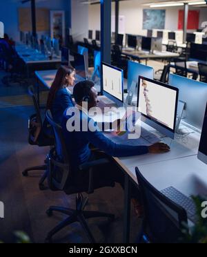 Deux directeurs travaillent dans le bureau de nuit, vue arrière.Hommes et femmes travailleurs, centre d'affaires sombre à l'intérieur sur fond, lieu de travail moderne Banque D'Images