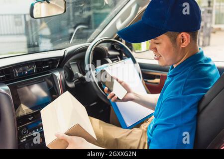 Un livreur asiatique en ligne tient les livraisons à l'intérieur des boîtes la voiture et l'utilisation du smartphone mobile pour vérifier la position à contacter le client pour Banque D'Images