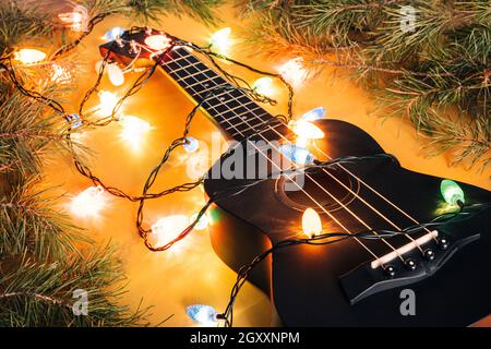 guitare ukulele noire et décorations de noël sur fond sombre. guitare hawaïenne avec guirlande lumineuse sur fond sombre.Guitare cadeau classique SH Banque D'Images