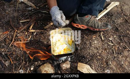 personne cuisinant des œufs frits dans la nature camping extérieur, cuisinière préparer le petit déjeuner pique-nique brouillé sur une poêle en métal. Banque D'Images