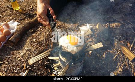 personne cuisinant des œufs frits dans la nature camping extérieur, cuisinière préparer le petit déjeuner pique-nique brouillé sur cuisinière en métal. Banque D'Images