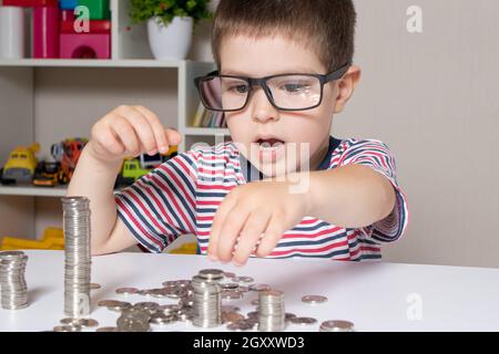 Un enfant en lunettes, un jeune homme d'affaires joue avec des pièces de monnaie et économise de l'argent. Banque D'Images