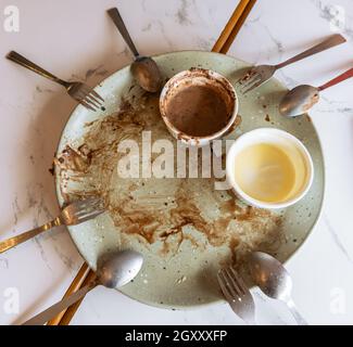 Vider l'assiette avec les restes de repas de dessert, les cuillères et les fourchettes sur une table en marbre.Assiette sale avec de la sauce au chocolat, du chocolat et de la glace à la vanille Banque D'Images