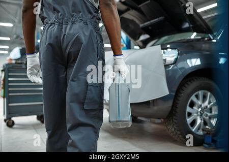 Un mécanicien de sexe masculin tient le réservoir d'huile, le service de voiture.Garage de réparation de véhicule, homme en uniforme, intérieur de poste automobile sur fond Banque D'Images