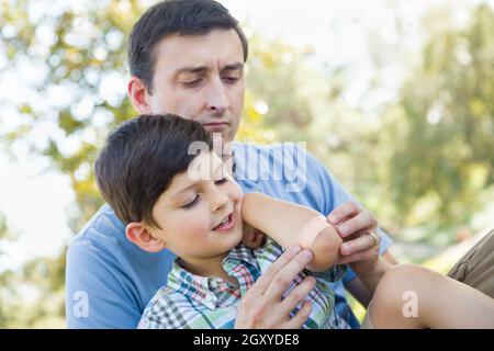 Père aimant met un bandage sur le coude de son jeune fils dans le parc. Banque D'Images