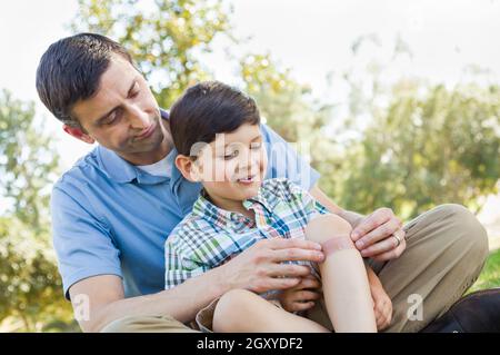 Père aimant met un bandage sur le coude de son jeune fils dans le parc. Banque D'Images