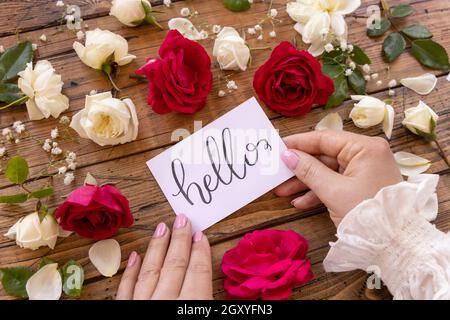 Femme mains tenant LA CARTE HELLO près des fleurs sur une table en bois gros plan Banque D'Images