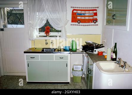 Une cuisine très basique dans un appartement ou un appartement dans une banlieue de Sydney, Nouvelle-Galles du Sud, Australie en 1973.Fait intéressant, bien qu'il soit mal équipé (avec seulement un petit plug-in, table de cuisson et grill), il contient deux éviers!Pour la décoration, il y a une torchon d'un bus londonien accroché au mur. Cette image est tirée d'une vieille transparence couleur amateur Kodak, une photographie vintage des années 1970. Banque D'Images