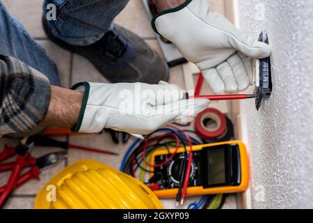 Vue de dessus. Un électricien au travail installe la prise électrique d'un système électrique résidentiel. Travailler en toute sécurité avec des gants de protection. Construire Banque D'Images