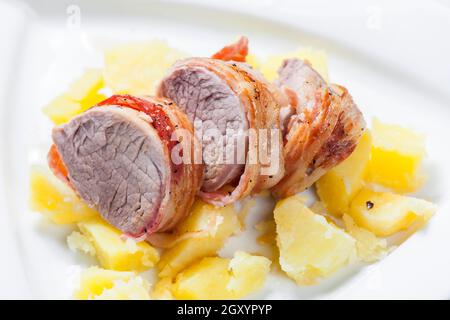 rouleau de porc emballé dans du bacon avec des pommes de terre Banque D'Images