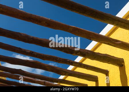 Poteaux en bois abstraits et mur jaune vif contre ciel bleu Banque D'Images