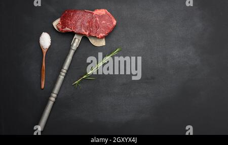 un morceau de bœuf cru est situé sur un couteau de fer, sur fond noir. Steak classique, espace copie Banque D'Images