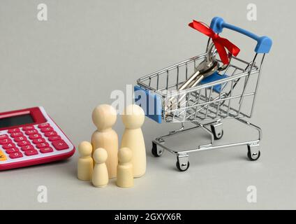 famille de figurines en bois et clés en métal dans un petit chariot rose sur fond gris. concept d'achat immobilier, loyer, hypothèque Banque D'Images
