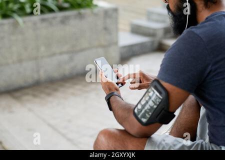 Vue sur l'épaule d'un jeune Indien avec une barbe en plein air et en utilisant l'application de fitness sur un smartphone Banque D'Images