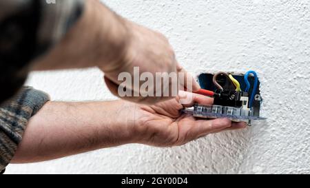 Un électricien fixe les câbles électriques dans les bornes de la prise d'un système électrique à l'aide d'un tournevis. Industrie de la construction. Banque D'Images