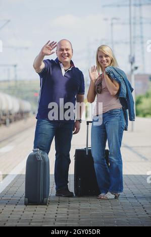 Couple heureux avec des stands de valises agitant sur une plate-forme, Allemagne Banque D'Images