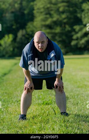 homme en surpoids debout épuisé dans un pré après qu'il fait du sport Banque D'Images