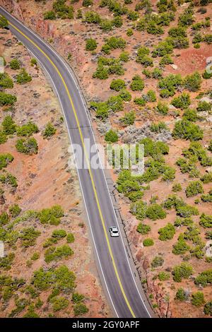 Vue en bas de la route qui se courbe dans le désert avec voiture blanche Banque D'Images