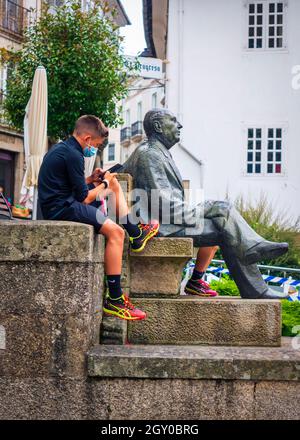 Mondoñedo, Lugo, Espagne.07,27,2021.Garçon utilisant son téléphone portable assis à côté de la statue du célèbre écrivain Alvaro Cunqueiro sur la place Banque D'Images