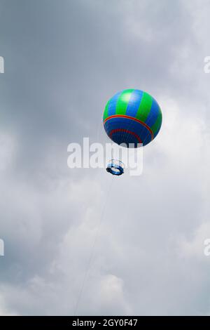 Un ballon d'air chaud bleu et vert s'élève dans un ciel nuageux et d'un gris inquiétant Banque D'Images