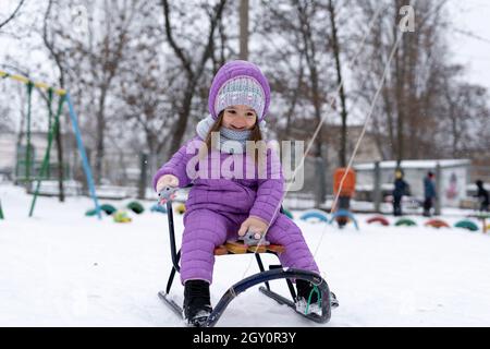 Portrait d'une fille heureuse.Un enfant en hiver est vêtu d'une veste violette pour faire de la luge pendant les vacances d'été. Banque D'Images