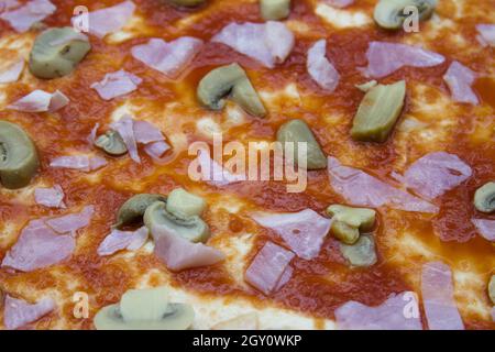 Gros plan d'une croûte de pizza crue assaisonnée de champignons roulés, de jambon en dés et de sauce tomate Banque D'Images