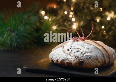 Stollen allemand traditionnel, branches à feuilles persistantes, guirlande sur une table de fête brune.Dessert traditionnel des fêtes de Noël. Banque D'Images