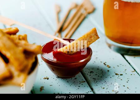 gros plan d'un petit bol en verre avec ketchup et une bande de poulet frit, trempée dans le plat, sur une table bleue à côté d'un bol avec plus de lanières de frit Banque D'Images