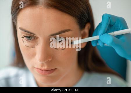 Le cosmétologue dessine des lignes sur le visage des femmes pour les procédures de levage Banque D'Images