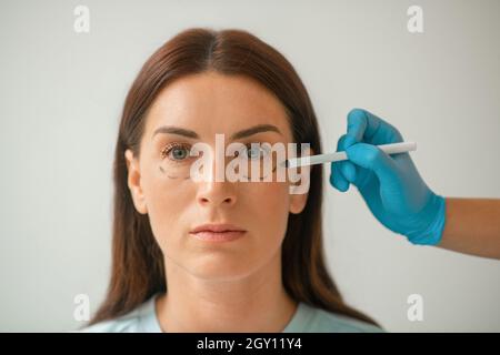 Le cosmétologue dessine des lignes sur le visage des femmes pour les procédures de levage Banque D'Images