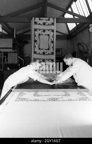 Zwei Mitarbeiter einer Textilfirma Stofbahn à Krefeld bedrucken eine mit einem Blumenmuster durch das Siebdruckverfahren, Deutschland 1930 er Jahre. Deux employés d'une entreprise textile à Krefeld sérigraphie d'un motif floral sur un panneau, l'Allemagne des années 1930. Banque D'Images