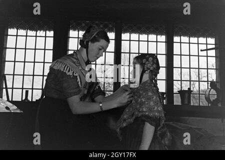 Eine Frau hilft einem kleinen Mädchen beim HANDBRAKE ! der Tracht der Gegend um Ammerland bei Bad Zwischenahn im Oldenburger Land, Deutschland 1930 er Jahre. Une femme d'aider une petite fille à porter le costume traditionnel de Ammerland près de Bad Zwischenahn au Oldenburg, Allemagne 1930. Banque D'Images