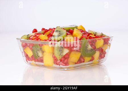 Fruits coupés mélangés disposés dans un bol en verre transparent avec fond blanc, isolé. Banque D'Images